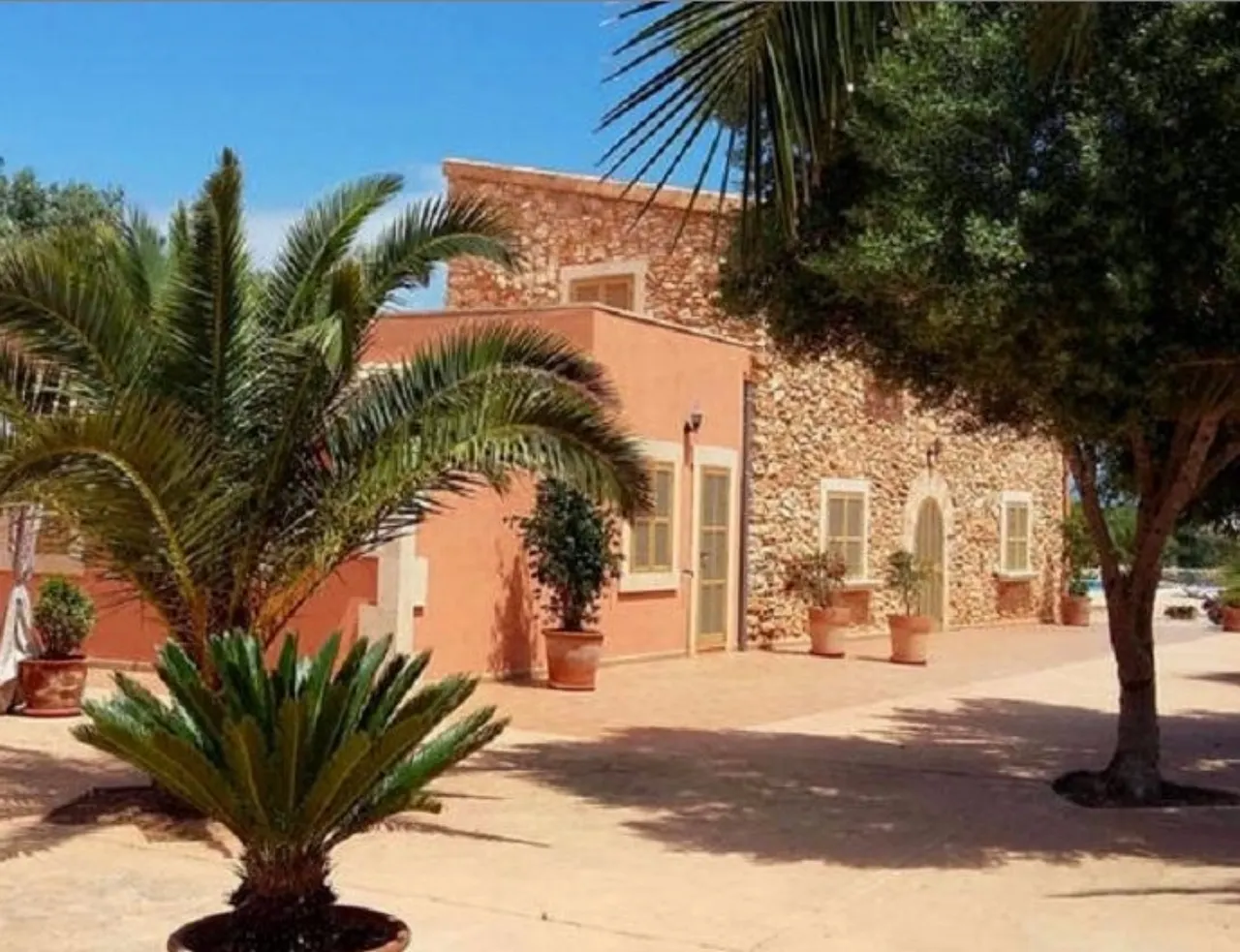 The terracotta-rendered wing of Finca Es Torrent den Cosme in daylight, framed by tall palms over a gravel courtyard