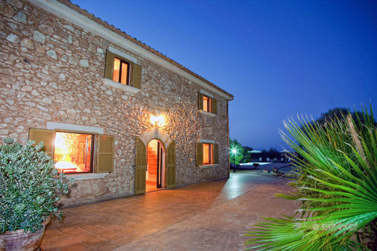 The dry-stone facade of Finca Es Torrent den Cosme at dusk, its windows lit warm against a deep blue sky