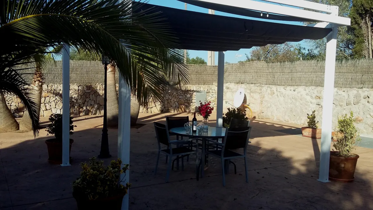 The pergola and a set table at dusk, warm light against the stone wall