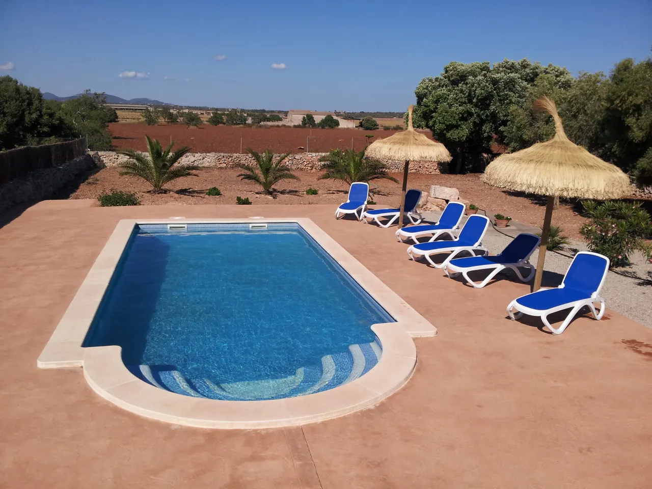 The pool seen across the terracotta deck, loungers in a row and low hills on the horizon