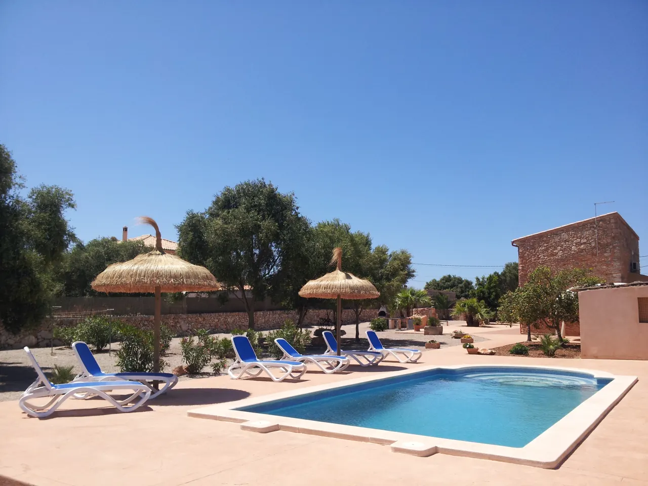 The pool with two thatched parasols, blue loungers and a low stone tower behind
